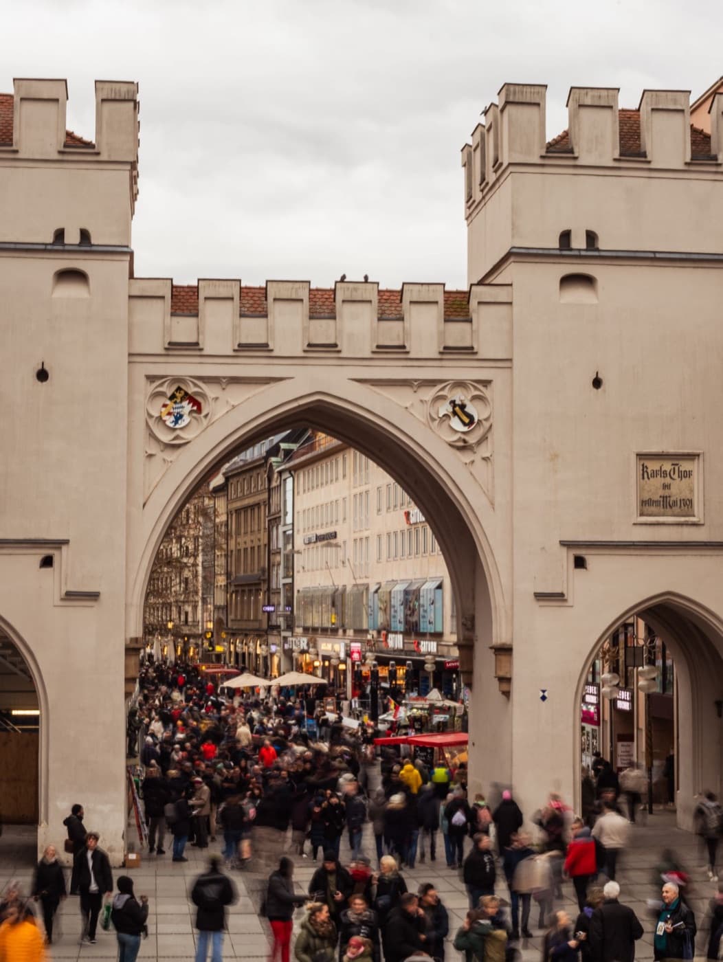 A crowded evening street scene through the medieval Karlstor gate in Munich